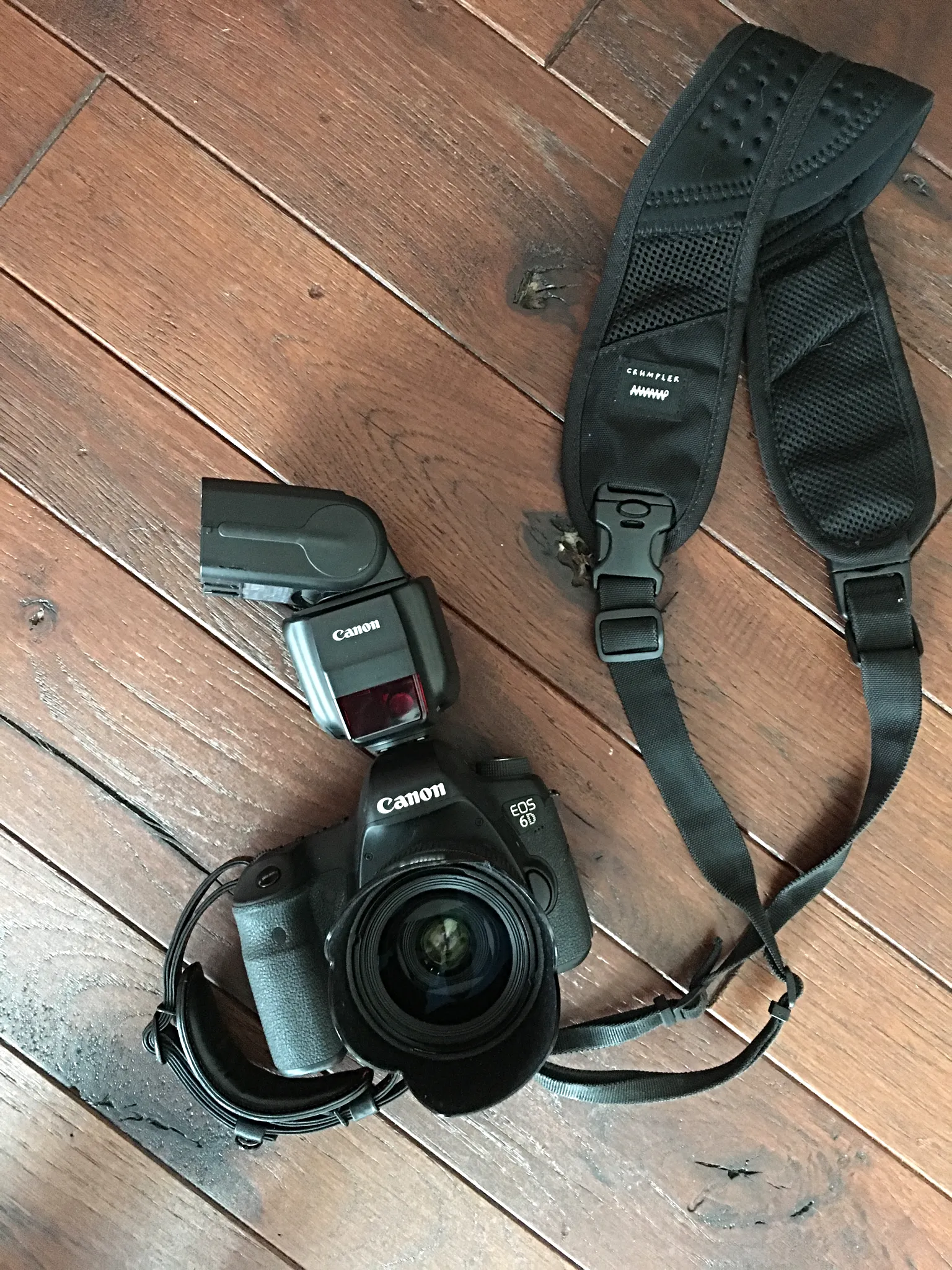Canon DSLR with a speedlite and camera strap on a wood floor