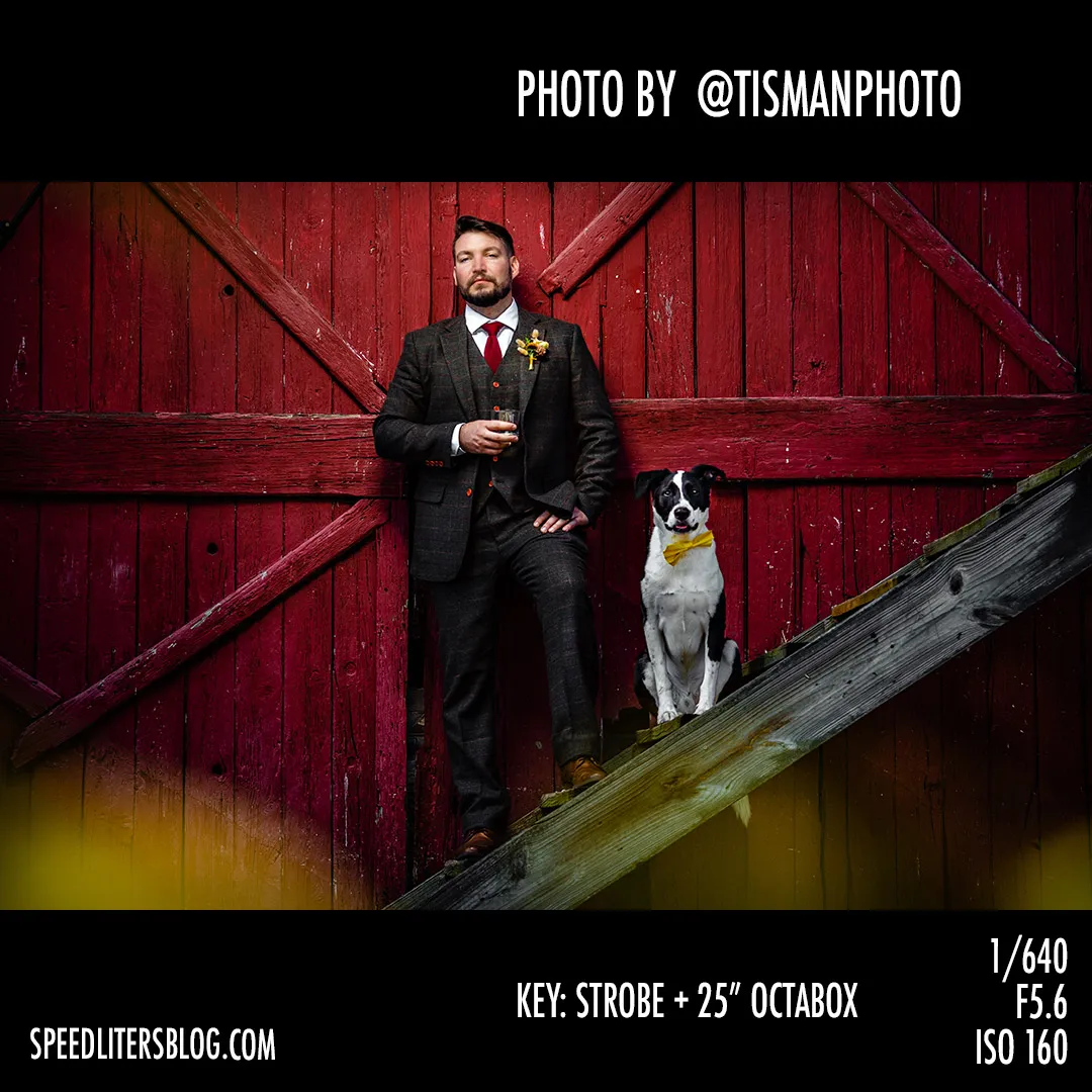 Groom in a three-piece suit with his dog in front of a red barn door, by Jeff Tisman