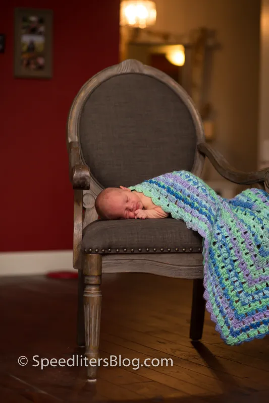 Newborn sleeping on an upholstered chair under a crocheted blanket